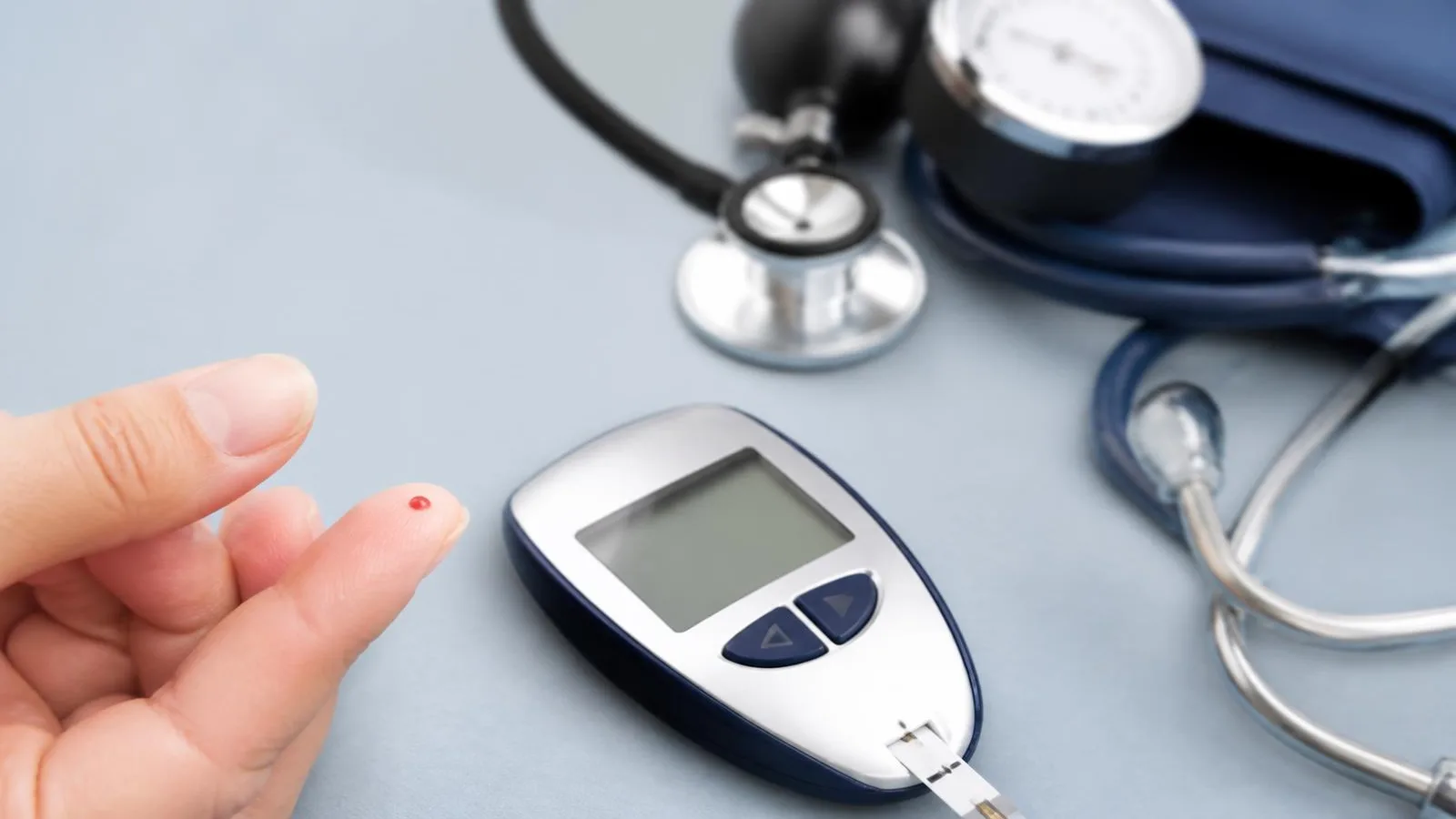 Blodsockermätare, blodtrycksmanschett och stetoskop på ljusblå bakgrund – kontroll av riskfaktorer vid diabetes